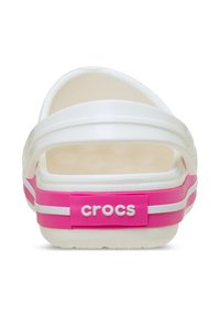 Witte Crocs-slippers met een roze hielband met witte strepen en logo, een ronde achterkant en een gladde, rubberachtige textuur.