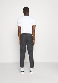 Pantalon à carreaux gris avec une coupe droite et une taille mi-haute, associé à un t-shirt blanc et des baskets blanches avec des accents verts.