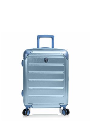 Maleta rígida de color azul claro con ranuras horizontales, asa extensible, cuatro ruedas giratorias y un pequeño logo en forma de escudo en el frontal.
