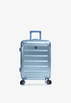 Maleta rígida de color azul claro con ranuras horizontales, asa extensible, cuatro ruedas giratorias y un pequeño logo en forma de escudo en el frontal.