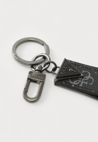 Black keychain with a textured rectangular strap, featuring a triangular metallic accent branded "Guess" and a silver-colored carabiner clip.