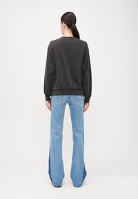 Mørkegrå hettegenser med ribbede mansjetter og nederkant, kombinert med lys blå flared jeans med sidespalter. Bakfra visning av antrekket.