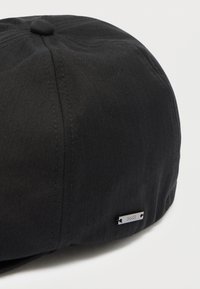 Čierna čiapka z textúrovaného materiálu s hladkým vrchom, zaobleným tvarom a malou kovovou značkou s nápisom "BOSS" na boku.