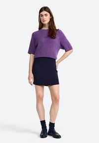 Purple, cropped, knitted sweater with short sleeves paired with a fitted navy mini skirt. Model wears black loafers and ankle socks.