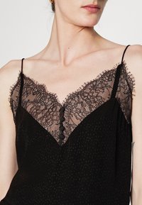 Černý top na ramínka s krajkovým lemováním na výstřihu, tenkými nastavitelnými ramínky a knoflíkovým detailem na přední straně. Hladká tkanina s jemnou strukturou.