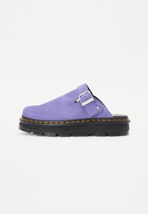 Sabots en daim violet avec une semelle noire robuste, ornés d'une boucle en métal argenté et d'une couture jaune contrastante le long de la base.