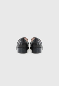 Chaussures en cuir noir avec une texture lisse, un bout arrondi, un petit talon carré et des détails de couture subtils à l'arrière.