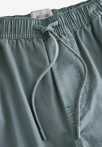 Grønne shorts med elastisk talje og snor, lavet af glat stof med synlige sømme og et mærke øverst.