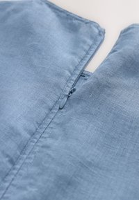 Un tissu en lin bleu clair présente une texture subtile. Une fermeture éclair centrale s'étend verticalement, avec une finition soignée le long des bords.