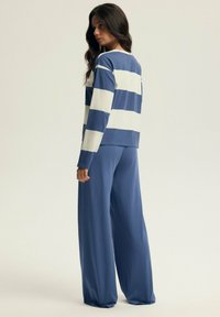 Niebieska i biała pasiasta koszula z długim rękawem i okrągłym dekoltem, zestawiona z niebieskimi spodniami o szerokich nogawkach, uszytymi z miękkiego, lekkiego materiału.