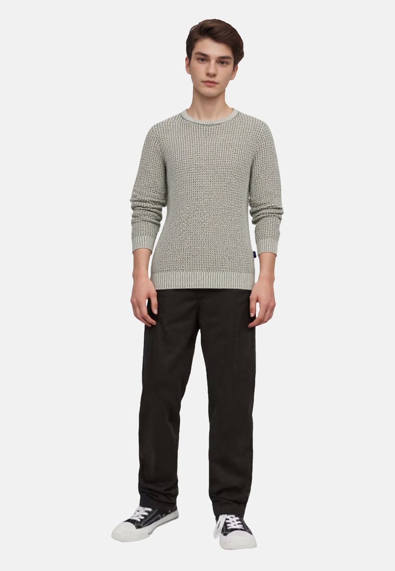 Hellgrauer strukturierter Strickpullover mit rundem Hals und gerippten Bündchen, kombiniert mit schwarzen Hosen und schwarz-weißen Sneakers.