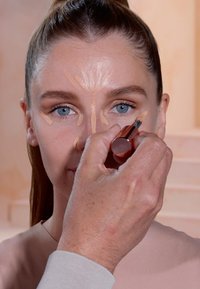 Makeupapplicatieproces met een crème concealerstick op de huid. Lichtbeige tint aangebracht in een contourpatroon op het gezicht.