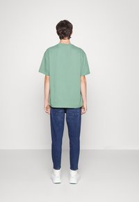 T-shirt de algodão verde com decote redondo, acompanhado de jeans slim-fit azul escuro. O conjunto é complementado com ténis brancos.