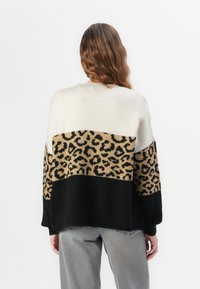 Gehaakte trui met een color-block ontwerp: crème, tan met luipaardprint en zwart. Zachte textuur met een relaxed fit en lange mouwen.
