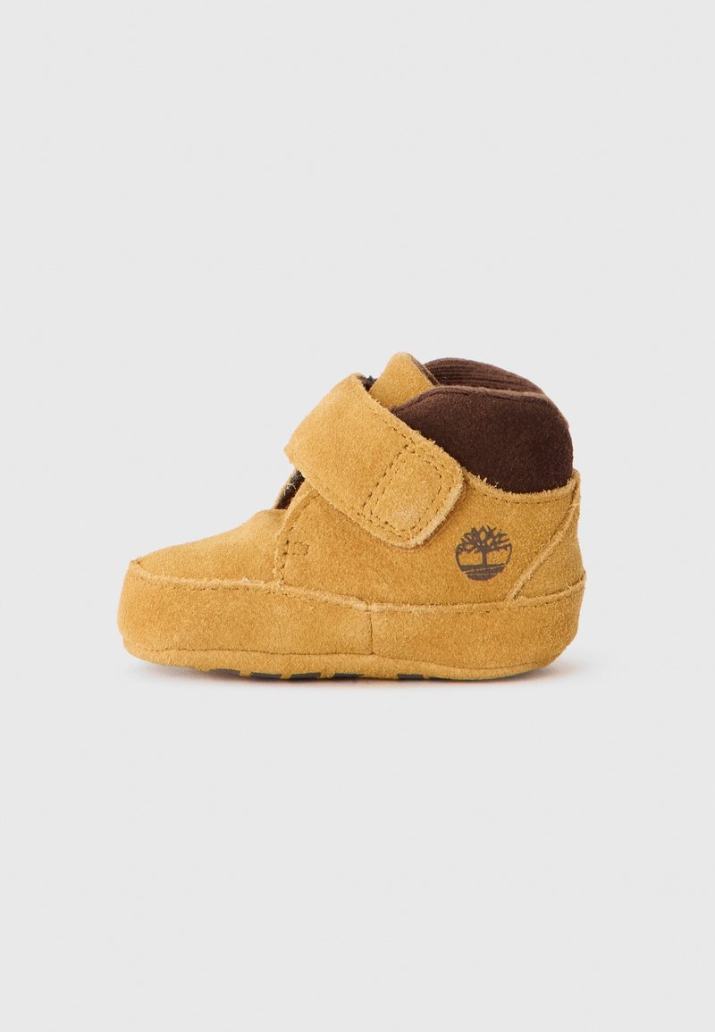 Chaussure bébé en suède marron et beige avec bride velcro et col matelassé à la cheville, avec un logo d’arbre sur le côté.