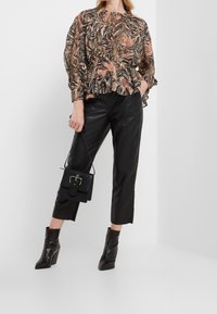 Blouse à manches longues avec un motif floral et de feuilles dans des tons pêche et noir, associée à un pantalon en cuir noir et des bottes noires à talons.
