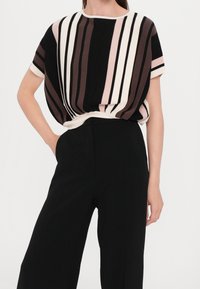 Randig topp i svart, beige och ljusrosa med korta ärmar och en lös passform, kombinerad med skräddarsydda svarta byxor.