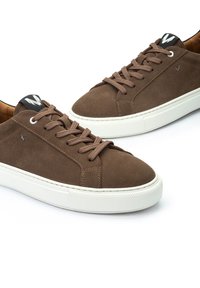 Baskets en daim marron avec semelle en caoutchouc blanche, bout rond et lacets texturés. Présente une étiquette logo noire sur la languette.