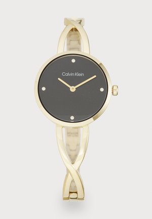 Montre dorée avec un cadran noir rond, quatre strass, et de aiguilles dorées minimalistes. Présente un design de bracelet en métal entrelacé.