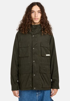 Chaqueta de color verde oscuro hecha de una tela texturizada, con un cuello alto, botones de presión en la parte delantera y cuatro grandes bolsillos. Diseño simple y funcional.