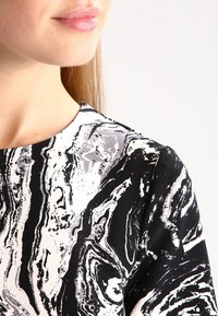 Černobílá abstraktní látka s vzory, na které se nacházejí víry a mramorování. Detailní záběr na výstřih a rameno s hladkým povrchem.