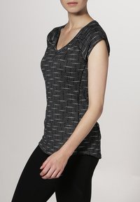 Svart och vit kortärmad topp med v-ringning, med ett texturerat mönster av prickar och en lätt figurnära passform.
