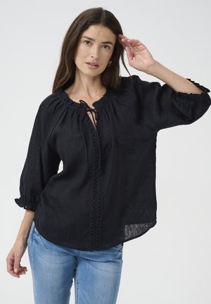 Blusa nera in lino con scollatura rotonda, dettaglio arricciato e maniche a sbuffo. Presenta un'apertura centrale con bordo in pizzo e lacci regolabili.