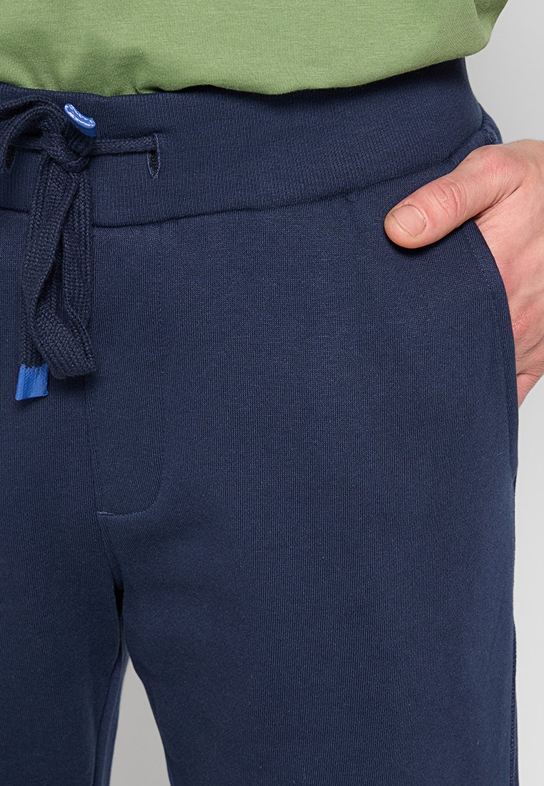 Pantaloni della tuta blu navy con tessuto testurizzato, dotati di una vita con cordino e tasche laterali. Decorati con una punta blu sul cordino.