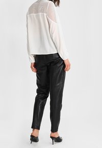 Vit blus med texturerad mesh på baksidan, kombinerad med svarta läderbyxor med avsmalnande ben. Outfiten har långärmade ärmar och är skräddarsydd i passformen. Svarta högklackade skor.