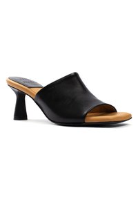 Mule aperti in pelle nera con un design curvo, dotati di un sottopiede beige e di un tacco corto e cilindrico. Texture liscia, dettagli ridotti al minimo.