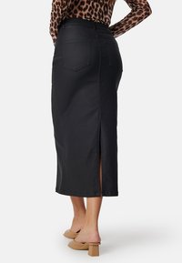 Zwarte denim midi-jurk met een rechte snit, zijslit en achterzakken, gecombineerd met beige block-heeled schoenen.