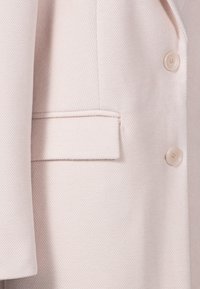 Ljusrosa jacka i ett texturerat tyg, med en enda bröstficka och två knappar, som visar en ren och skräddarsydd design.