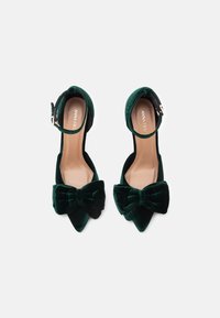Zöld bársony magassarkú cipők hegyes orral, bokapánttal és nagy masnival elöl. Simas texture világos bézs talpbéléssel.