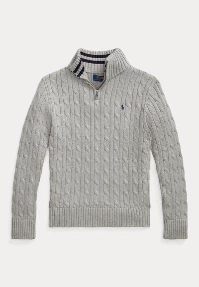 Svetra svetlo siva barva, pletena iz vzorca kabel, z visokim ovratnikom in zadrgo. Ima rebrast rob in manšete, z notranjim ovratnikom v mornarsko modri in beli črtasti vzorec.