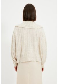 Béžový žebrovaný svetr s širokým límcem, spadlými rameny a zkráceným střihem, vyrobený z měkkého materiálu s jemnou texturou.