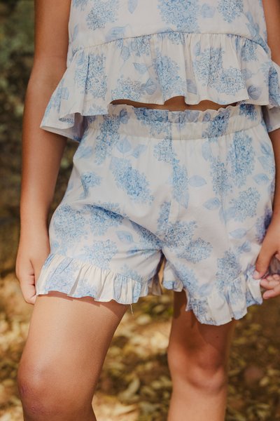 Lett bomullsantrekk med rynkete topp og shorts. Hvit bakgrunn med blå blomster mønster. Shorts har rynkete kant.