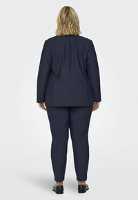 Námořnický dvoudílný oblek, který obsahuje přizpůsobenou blazer s vycpávkami na ramenou a slim-fit kalhoty. Hladká tkanina s jemným leskem a bez viditelných vzorů.