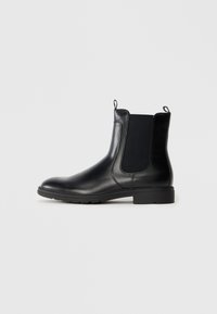 Botas Chelsea de cuero negro con paneles laterales elásticos, puntera redondeada y tacón bajo en bloque. Presentan lengüetas para ponerlas y soltarlas fácilmente.