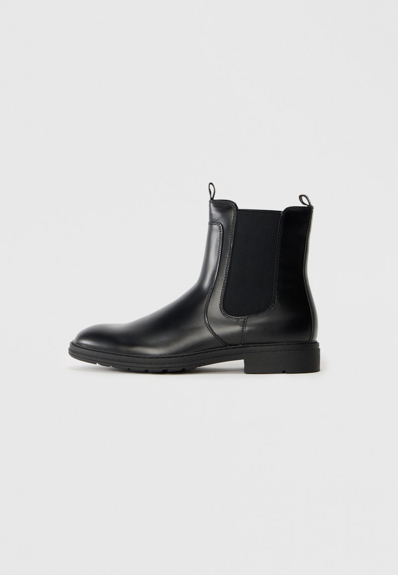 Botas Chelsea de cuero negro con paneles laterales elásticos, puntera redondeada y tacón bajo en bloque. Presentan lengüetas para ponerlas y soltarlas fácilmente.