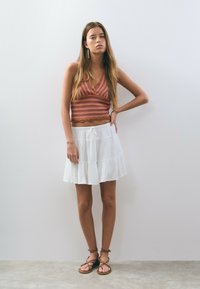 Top de punto sin mangas en tonos rojos y rosas, combinado con una falda blanca en capas, adornada con un cordón. Lleva sandalias marrones de tiras.