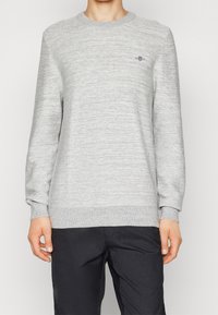 Sweatshirt gris avec un motif de tricot texturé, encolure ronde et poignets côtelés. Présente un petit logo brodé sur la poitrine.