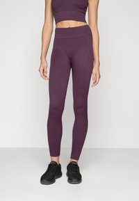 Lila bordázott leggings, testre simuló dizájnnal, magas derékkal és bokáig érő szabással, fekete sportcipőkkel párosítva.