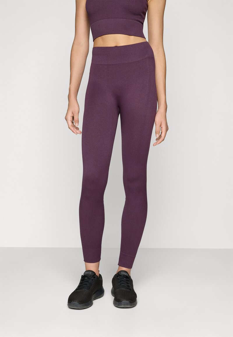 Lila bordázott leggings, testre simuló dizájnnal, magas derékkal és bokáig érő szabással, fekete sportcipőkkel párosítva.