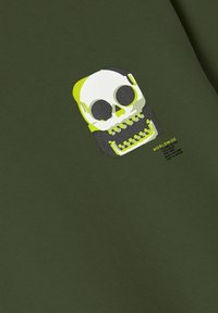 Tessuto verde oliva con un grafico di un teschio in bianco e accenti gialli. Il design include del testo sotto il teschio in un font moderno.