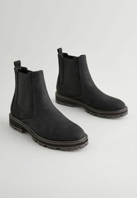 Botas Chelsea negras con paneles laterales elásticos y lengüetas de tirón, que cuentan con una parte superior texturizada y una suela exterior resistente para mayor tracción.
