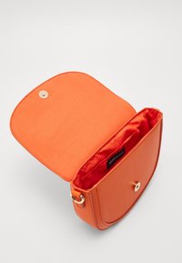 Borsa sintetica arancione con chiusura a patta arrotondata e hardware dorato. L'interno presenta una fodera in tessuto morbido e un'etichetta con logo.
