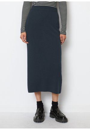 Frau trägt einen marineblauen Midirock, schwarze klobige Loafers mit schwarzen Socken und ein schwarz-weiß gestreiftes langärmeliges Oberteil.
