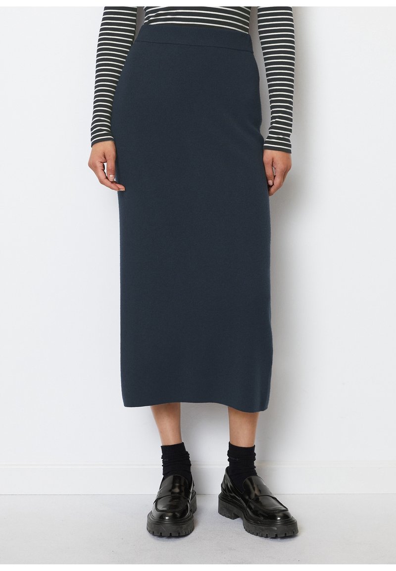 Femme portant une jupe midi bleu marine, des mocassins noirs épais avec des chaussettes noires et un haut à manches longues rayé noir et blanc.