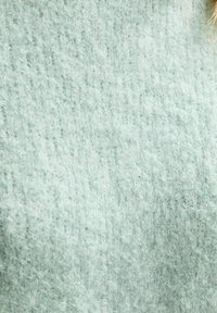 Ljus mintgrön stickad tyg med en strukturerad, fluffig yta. Mönstret är subtilt och visar en mjuk, varm känsla.