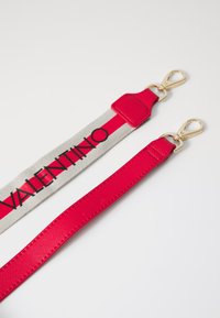 Piederums ar platu sarkanu neilona siksnu ar pelēkiem akcentiem un melnu "VALENTINO" tekstu. Zelta krāsas sprādzes abos galos.